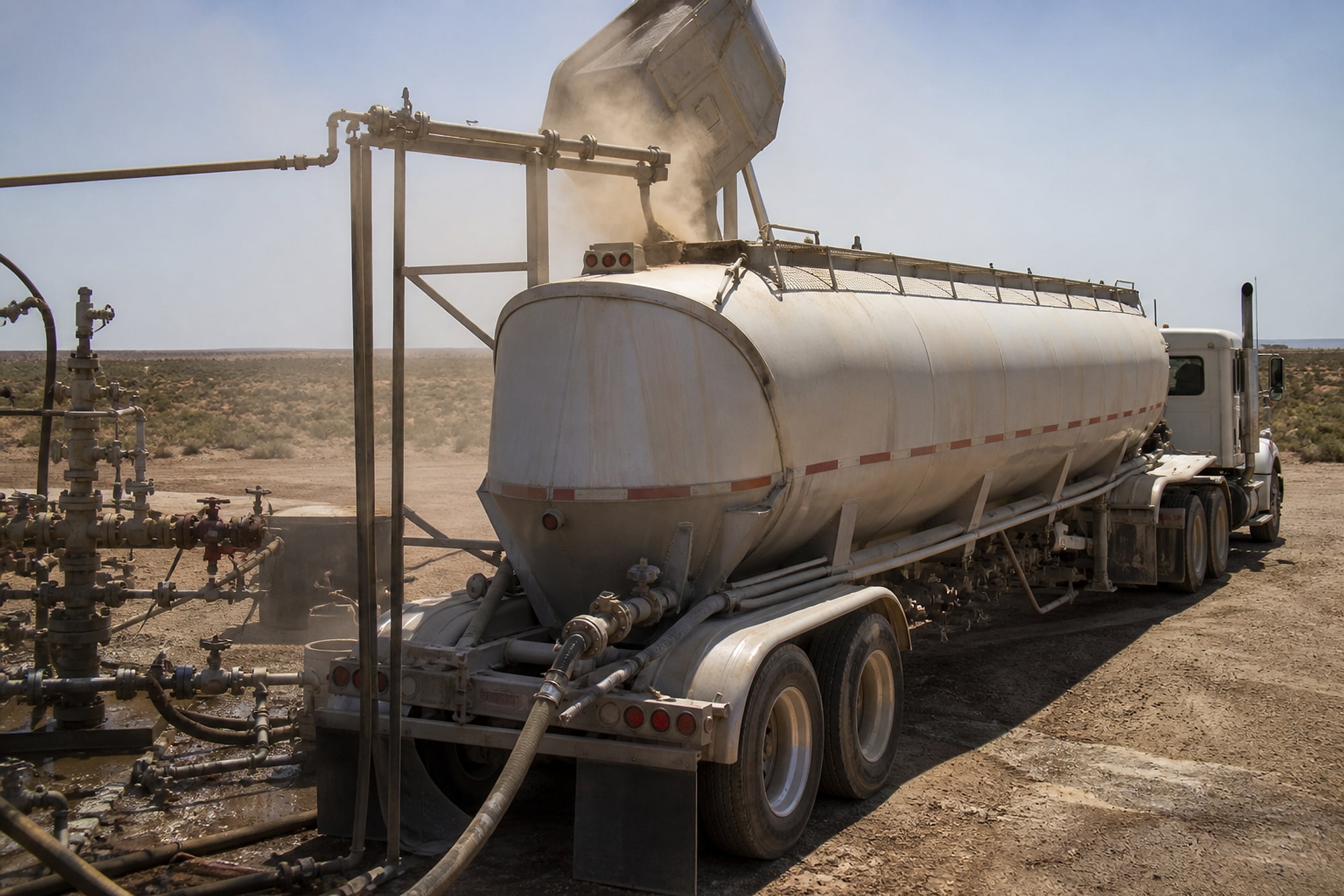 A pneumatic bulk trailer discharging frac sand at a West Texas well site